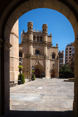 Main square of Castellon de la Plana through an arch with the Co-Cathedral of Santa Maria in the background on a sunny day with a blue sky, Spain