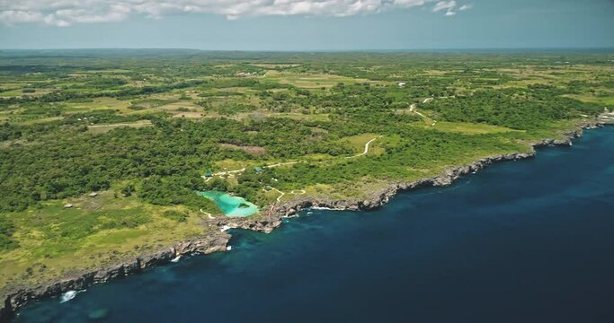 Cliff sea coastline with green landscape with limpid lake on top in aerial view. Scenic seascape admist tropic greenery nature at Weekuri lagoon, Sumba Island, Indonesia. Cinematic drone shot