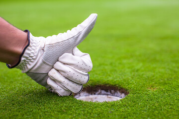 Men's hand in a glove golf shows OK near the hole