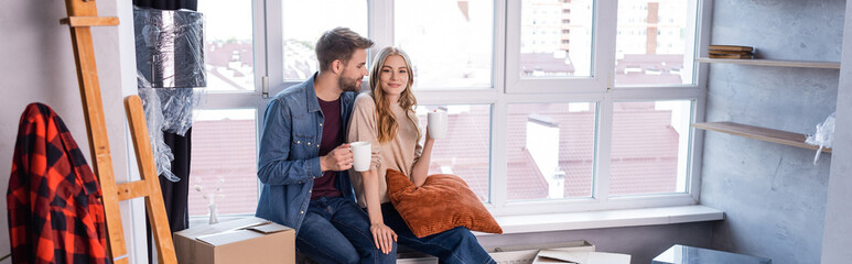 Obraz na płótnie Canvas website header of couple holding cups of tea near carton boxes, moving concept