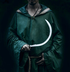 shaman wear green shroud and hold in hands sickle. green forest background.