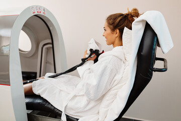 Smiling woman using oxygen mask during treatment in hyperbaric chamber.