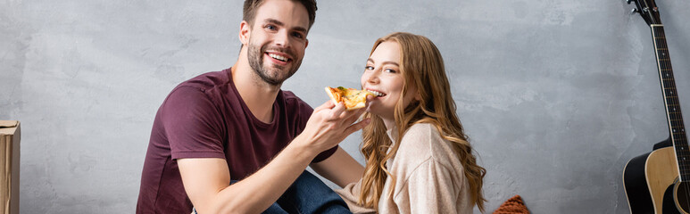 panoramic concept of pleased man feeding girlfriend with pizza