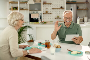 Happy mature man waving while making video call over digital tablet at home.