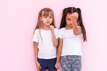 Image of two angry teenage girls with braids in casual clothes standing isolated over pink background