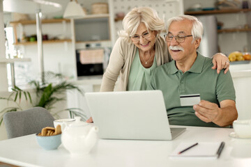 Happy mature couple using laptop and credit card while home shopping.