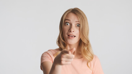 Young amazed woman showing index finger in camera isolated on wh