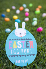 Easter egg hunt rabbit sign with scattered colorful eggs lying on the green grass hiden childhood adventure fun for the kids