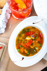 Traditional vegetable soup broth in a white plate on a table in a restaurant.