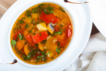 Traditional vegetable soup broth in a white plate on a table in a restaurant.