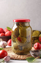 Marinated tomatoes with garlic in grape leaves in two glass jars on grey background. Closeup.