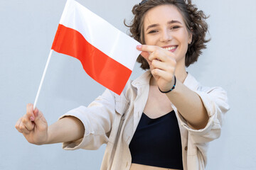 Young woman holding flag of Poland over gray background and looking at camera. Happy female student, learning Polish.