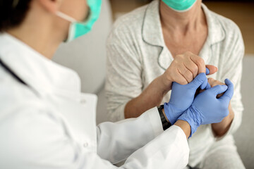 Close-up of a doctor and senior woman holding hands during home visit.