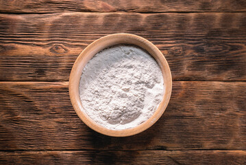 A flour in the wooden plate on the kitchen table background.