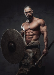 Muscular guy dressed like ancient viking posing in studio with dark background holding shield and...