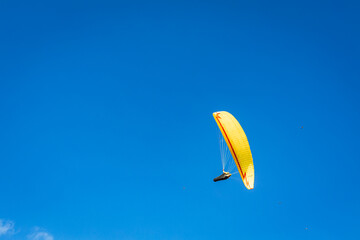 A paraglider with a bright yellow parachute against a clear blue sky