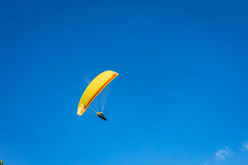 A paraglider with a bright yellow parachute against a clear blue sky