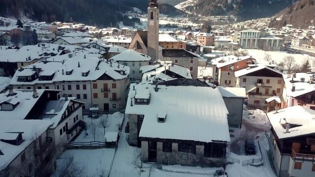 Pellizzano winter scene, small mountain village church covered in snow, aerial reveal