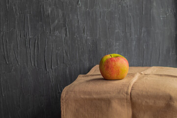 A lonely raw apple with a multi-colored skin lies on a brown cloth