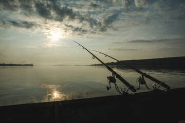 Silhouettes of the fishing rods against the side of a boat on a river in the early morning