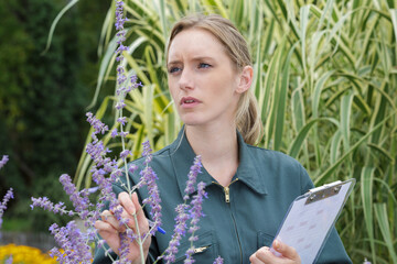woman with clipboard and pen writing and examining plants