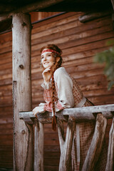 A beautiful Slavic girl with long blonde hair and brown eyes in a white and red embroidered suit stands on the porch of a house.Traditional clothing of the Ukrainian region.