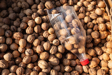 Top view of a box filled with walnuts on the market. On the foreground is a homemade bucket made of a plastic bottle with a red cap. Background. Texture.