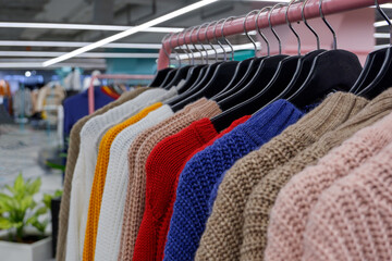 woolen sweaters of large knitting on hangers on the counter in the store. Shallow depth of field