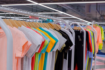 light summer t-shirts in different bright colors on hangers on the counter in the store. Shallow depth of field