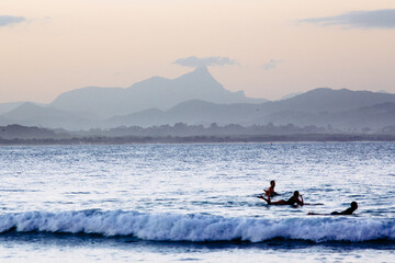 Mount Warning and surfers in the water at Byron Bay on dusk.