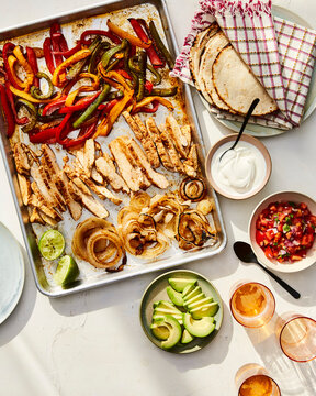 Overhead view of chicken fajitas with roasted vegetables in sheet pan and tacos served on table