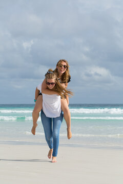 Teenage girls piggy backing on the beach