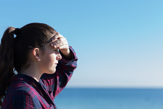 Teenage girl shading her eyes,looking out to sea