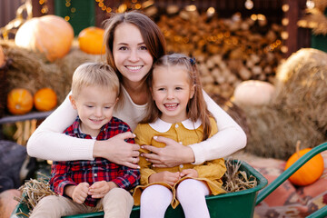 Cheerful family on the farm. Parenting and childhood. Motherhood. Autumn Thanksgiving Day. Outdoor games. Mom drives the children in a wheelbarrow. Harvesting at  farm. Vacation home. Yard decor