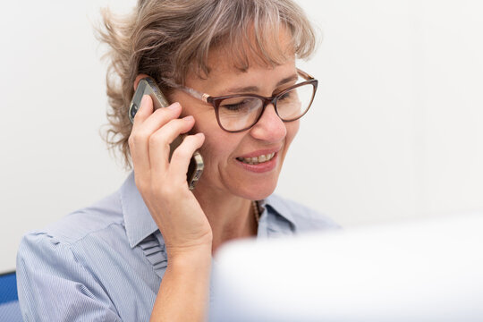 Woman in office behind computer screen with phone to ear
