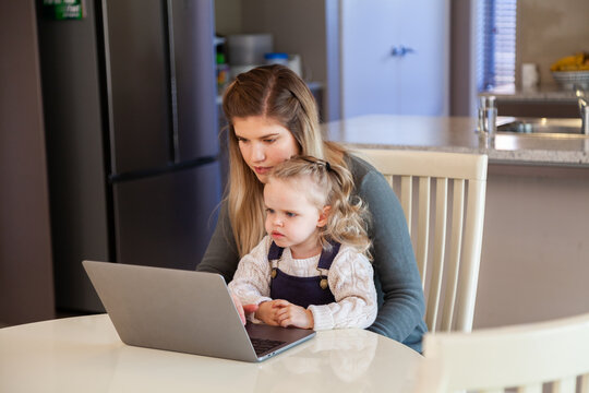 Young mother working from home on laptop with her little girl helping