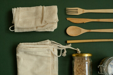 Zero waste kit. Set of eco friendly bamboo cutlery, mesh cotton bags, glass jars with a nuts. Plastic free lifestyle concept. Natural and reusable items accessories on green surface.