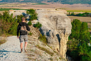 Naklejka premium Young man in jacket walking on narrow path on mountain range