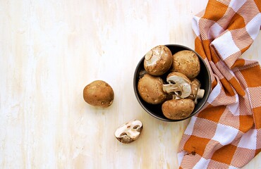 Obraz na płótnie Canvas Whole and cut brown mushrooms in a clay bowl on a light concrete background. Cooking ingredients. Culinary background.