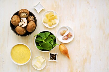 Prepared ingredients for cooking polenta with fried mushrooms and stewed spinach on a light concrete background. Step by step recipes. Polenta and corn grits recipes.
