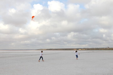 Obraz premium girl and boy running on pink salt lake with orange kite