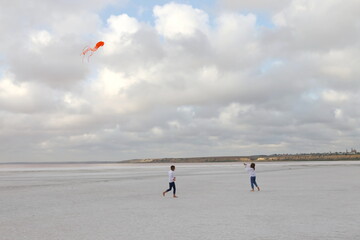 girl and boy running on pink salt lake with orange kite