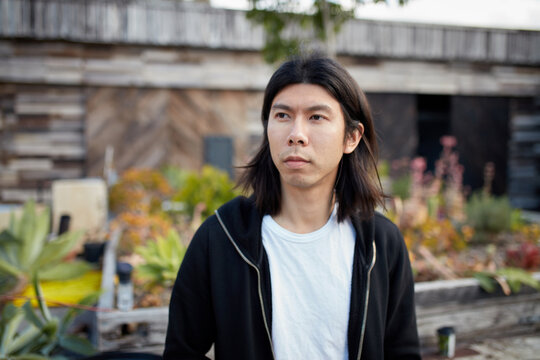 Young Asian man with long hair standing outside in courtyard