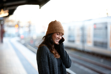 Young woman waiting at train station talking on mobile phone