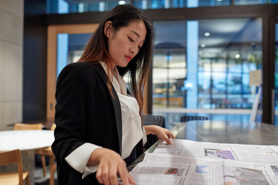 Young Asian business woman drinking coffee and reading newspaper