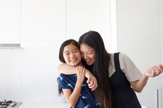 Portrait of smiling mother embracing her daughter in kitchen
