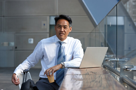 Asian businessman having a coffee whilst using laptop