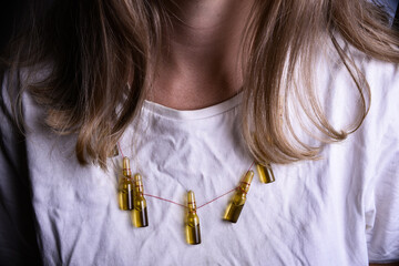 Woman in medical mask and white t-shirt. Woman wearing jewelry of medical ampoules.Close- up of a young woman with a surgical mask on her face 