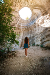 Light rays hitting on young adventure woman tourist inside deep cave with a open hole