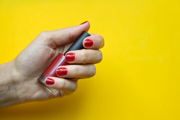 Girl holding red nail polish in hand with painted nails